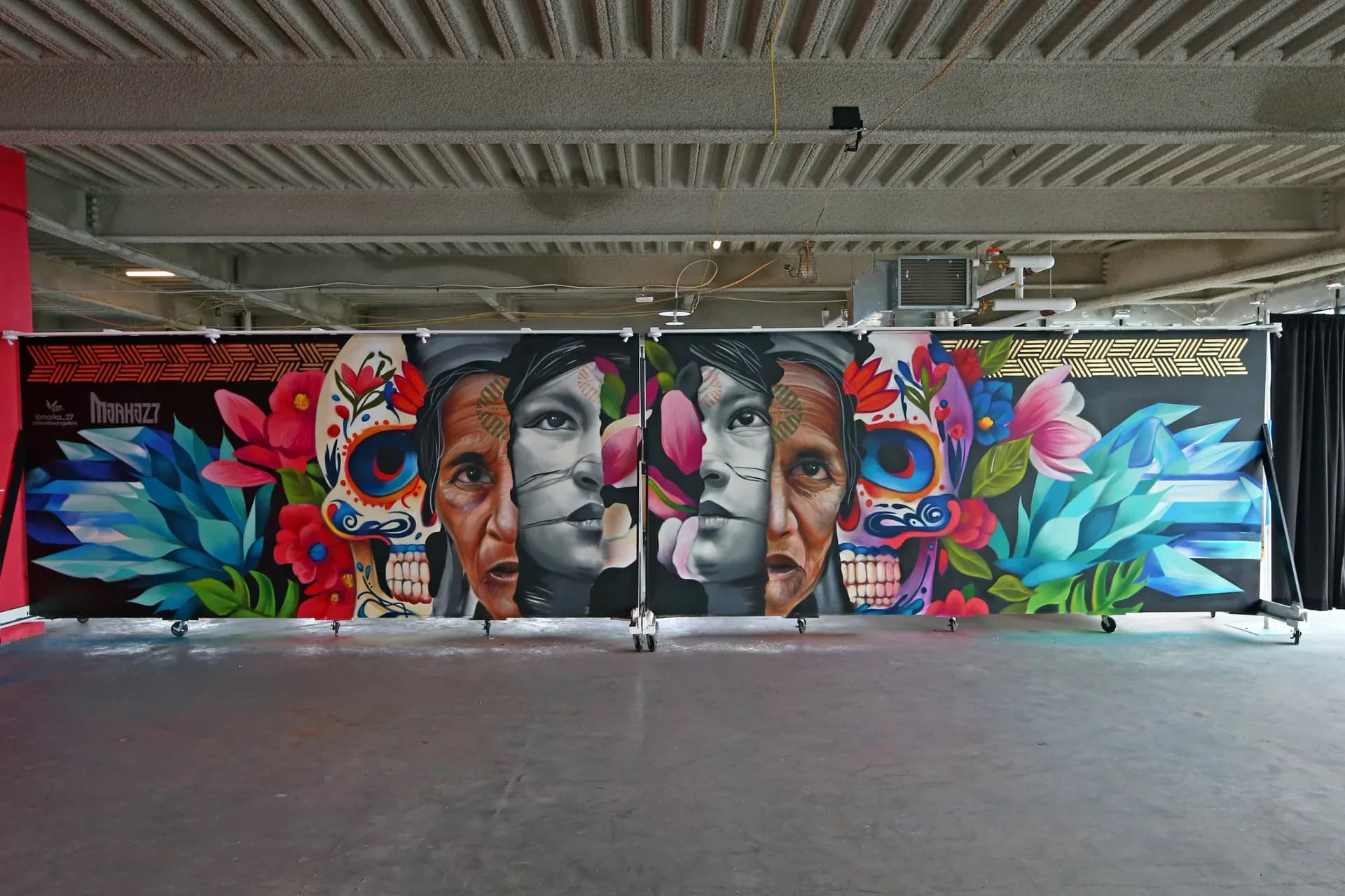 Large-scale building mural featuring two Indigenous women warriors with a swirling blue water globe, feathers, butterflies, and botanical elements