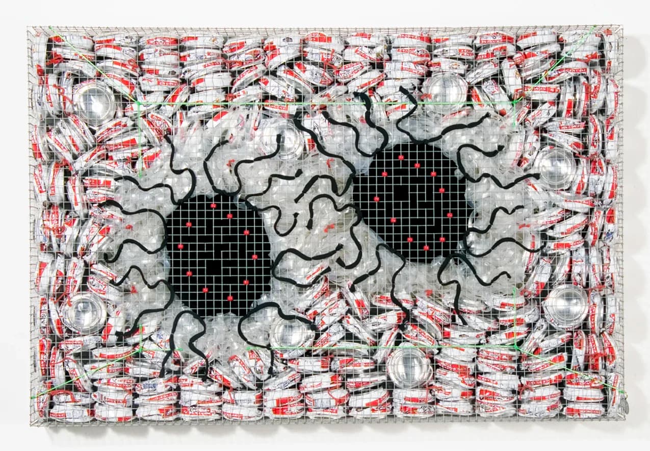 Large mixed-media wall sculpture made of crushed aluminum cans and wire mesh with black painted lines forming eye-like voids