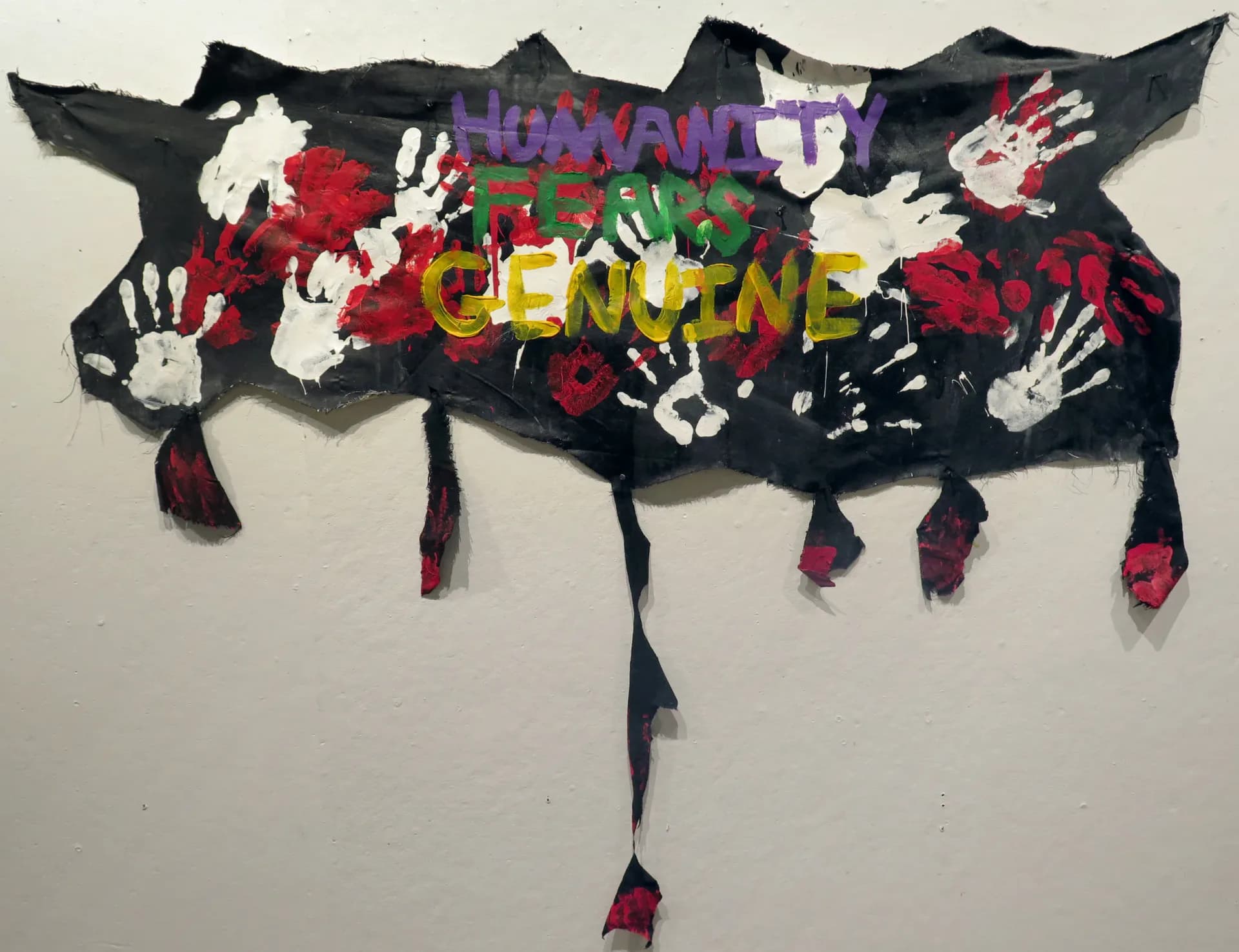 Textile or fabric artwork shaped like a cloud with colorful painted text and hand motifs on black background, with dangling ribbon strips.