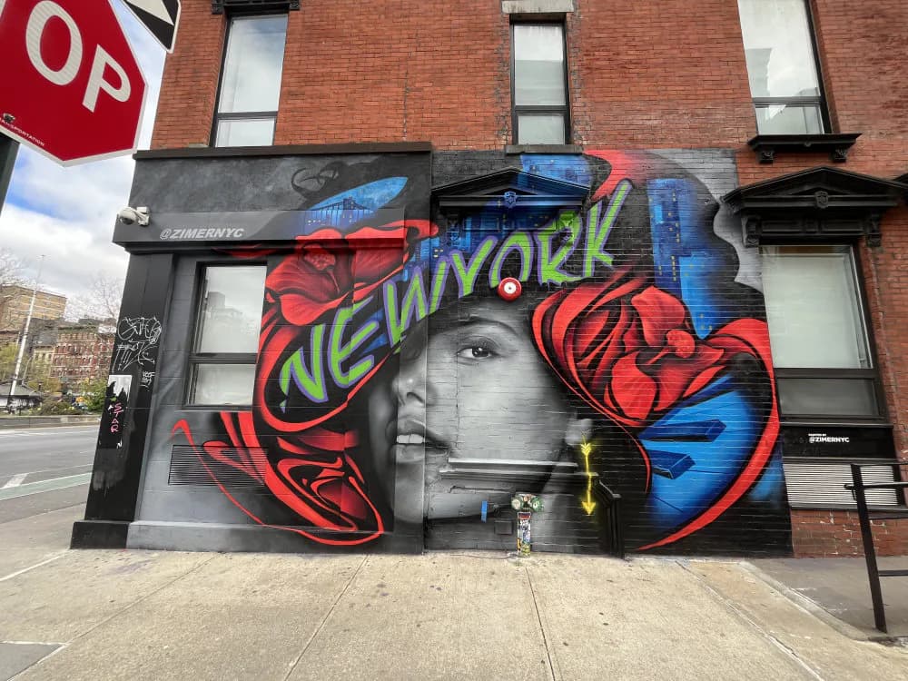 Street mural combining grayscale portrait with vibrant red, blue, and green abstract lettering reading 'NEW YORK' on brick building.