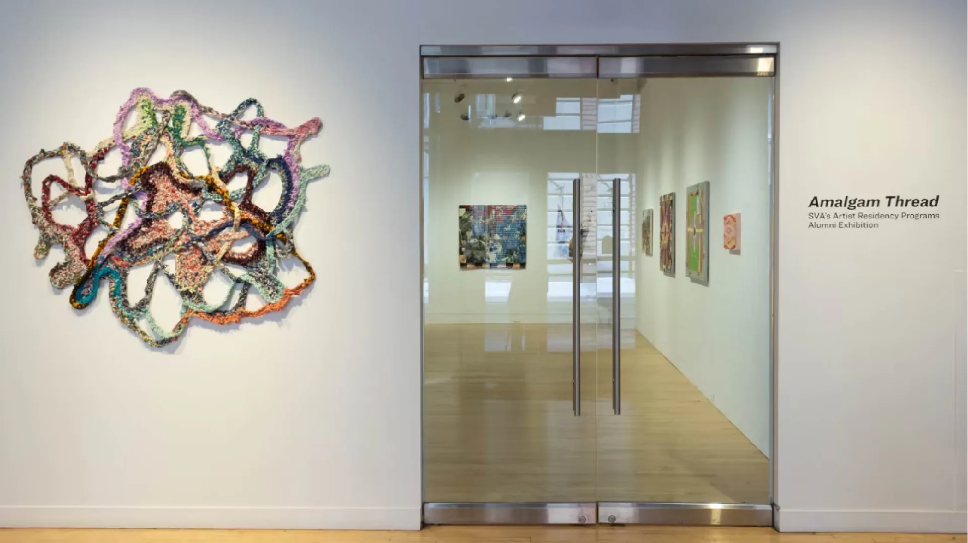 Colorful crochet/fiber wall sculpture with intertwining forms displayed near gallery entrance