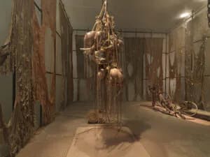 Gallery interior displaying multiple hanging sculptural installations in natural materials and fibers suspended from ceiling and walls, neutral tones throughout.