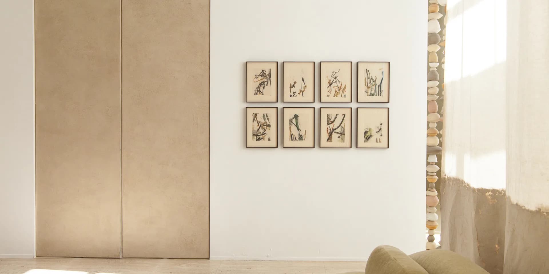 Minimalist gallery interior with beige wall panels, eight framed botanical drawings arranged in grid, natural light from window.