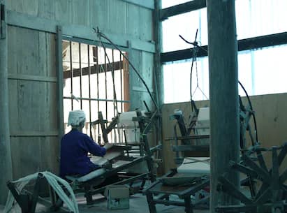 Person working at desk in dilapidated industrial space with metal structural beams and barred windows.