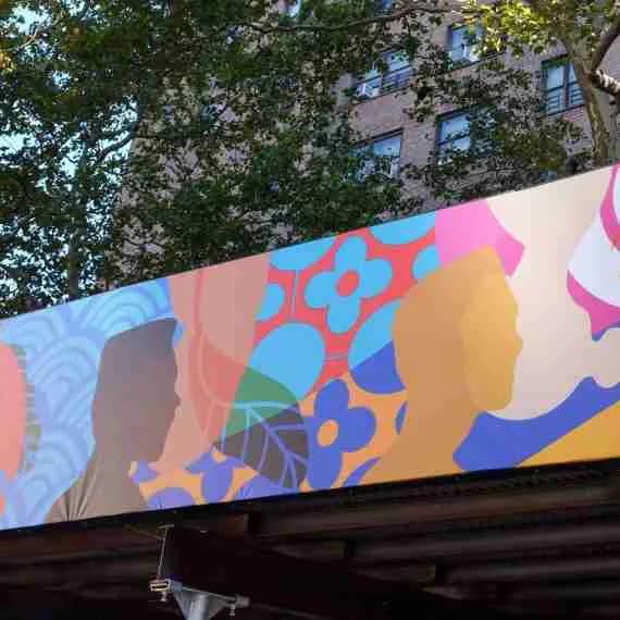 Colorful mural featuring stylized profile silhouettes in pink, blue, yellow, and orange with geometric patterning on a beige background.