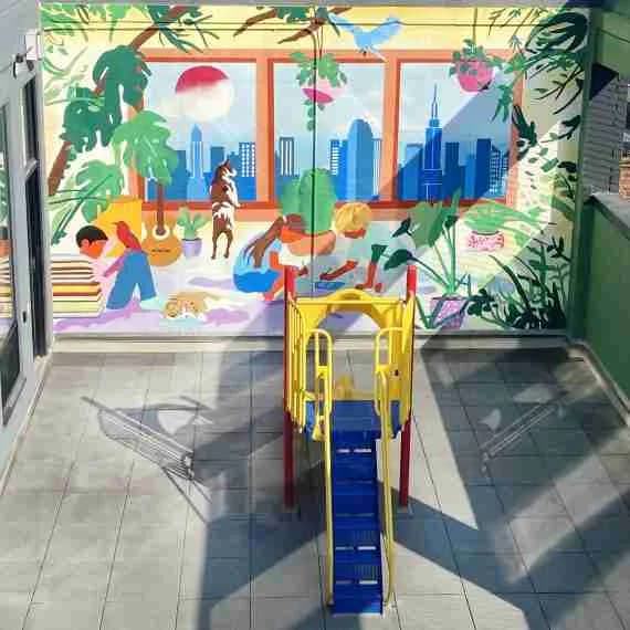 Vibrant mural visible through glass doors showing people relaxing indoors with plants, geometric shapes, and a blue cityscape beyond the windows.
