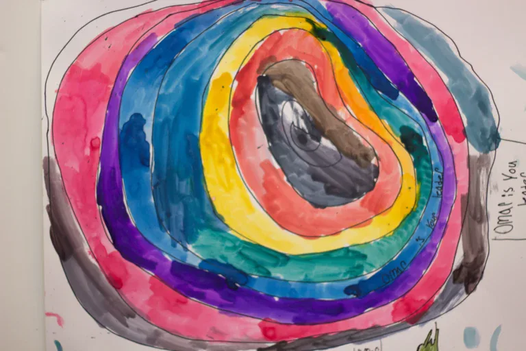 Concentric colored circles in watercolor or markers—pink, blue, yellow, red, purple—creating a mandala-like target pattern on paper.