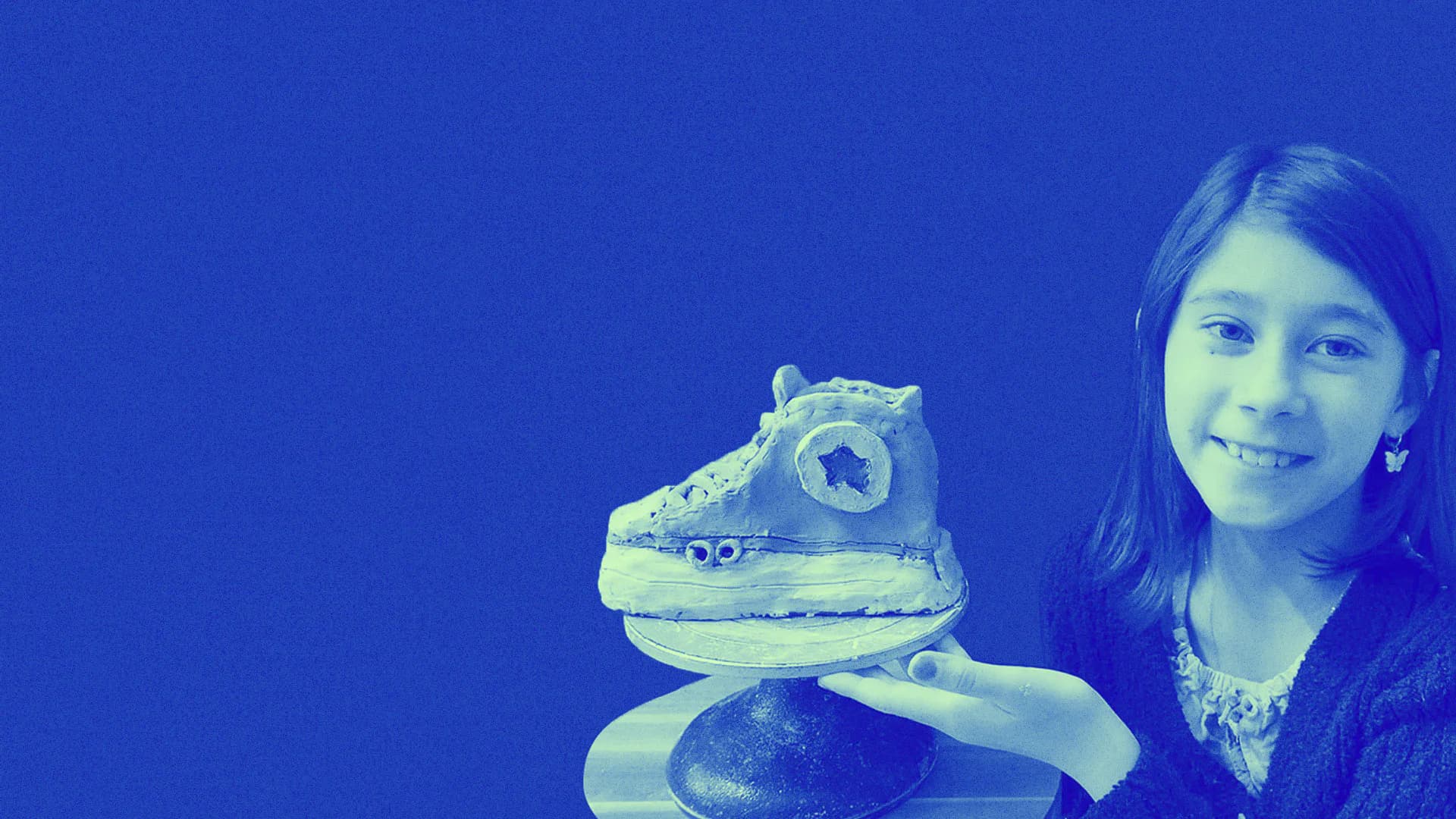 Monochromatic blue-toned photograph of smiling person holding sculptural ceramic piece resembling stylized animal form.