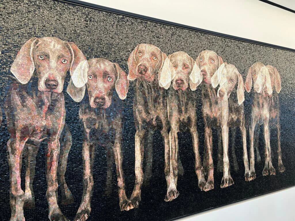 Textile or tapestry depicting eight dogs in varied brown and light tones arranged in a row against dark background.
