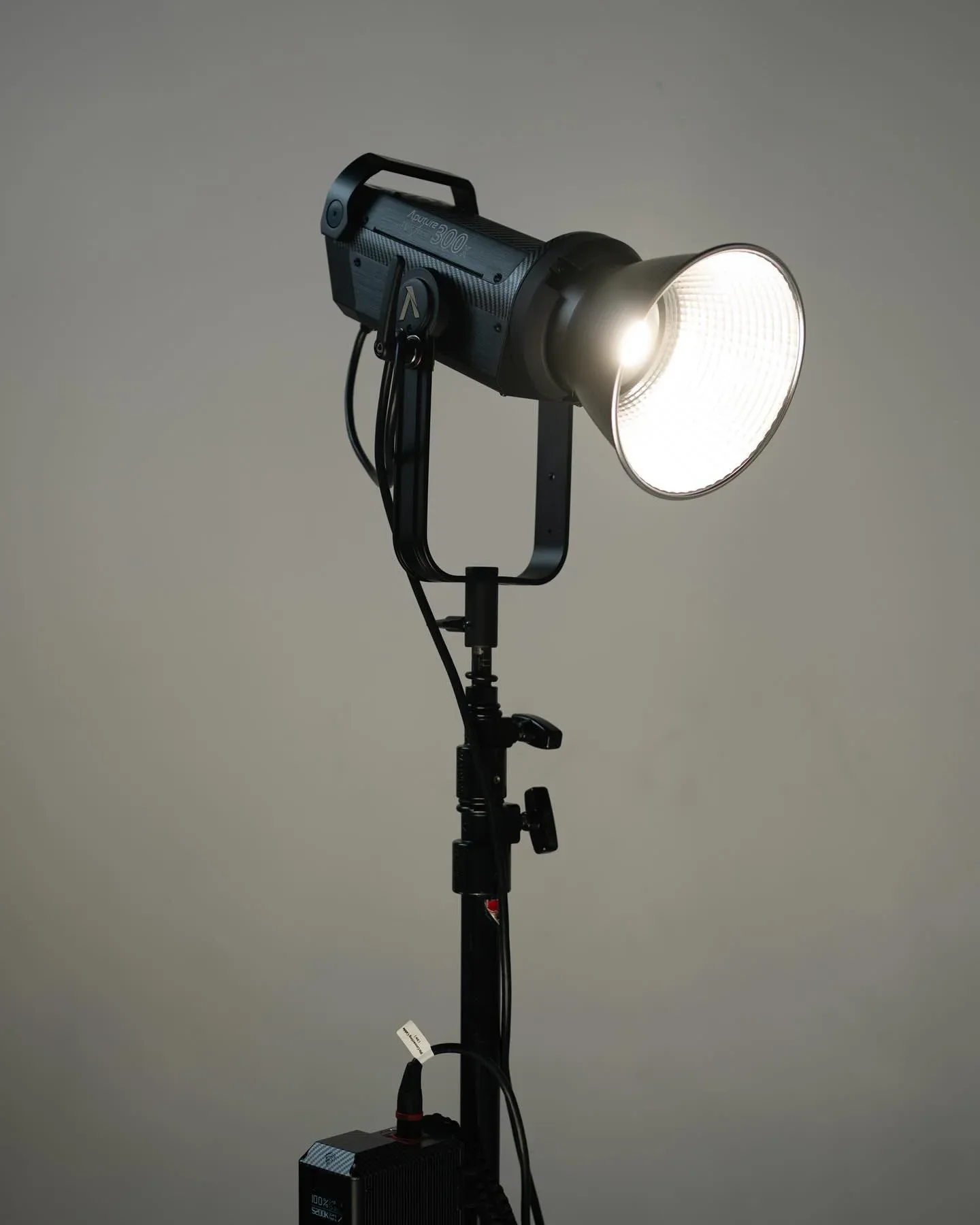 Professional film/studio light fixture mounted on stand with broad white reflector and black housing.