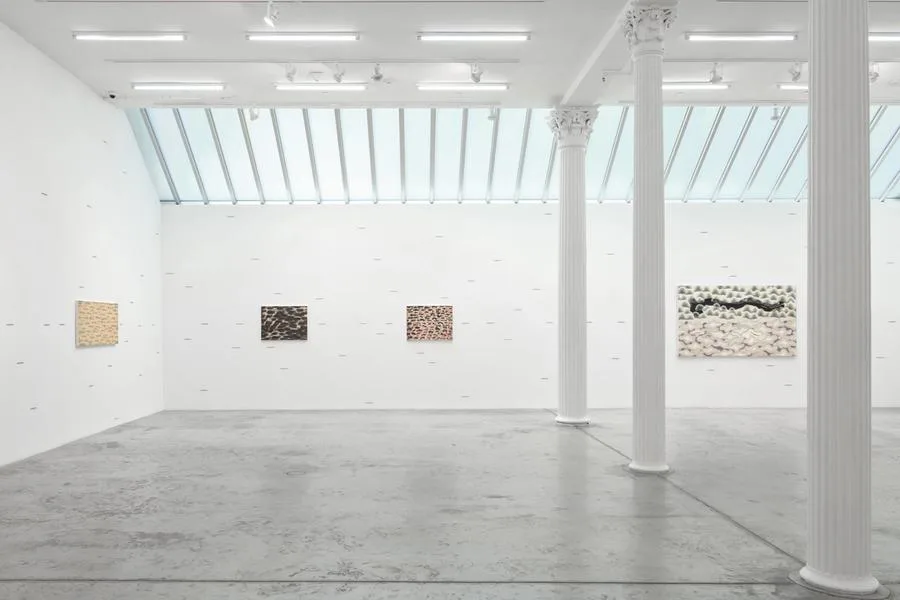 Bortolami gallery interior with polished concrete floor, white walls, skylights, and four abstract artworks on display alongside architectural columns.