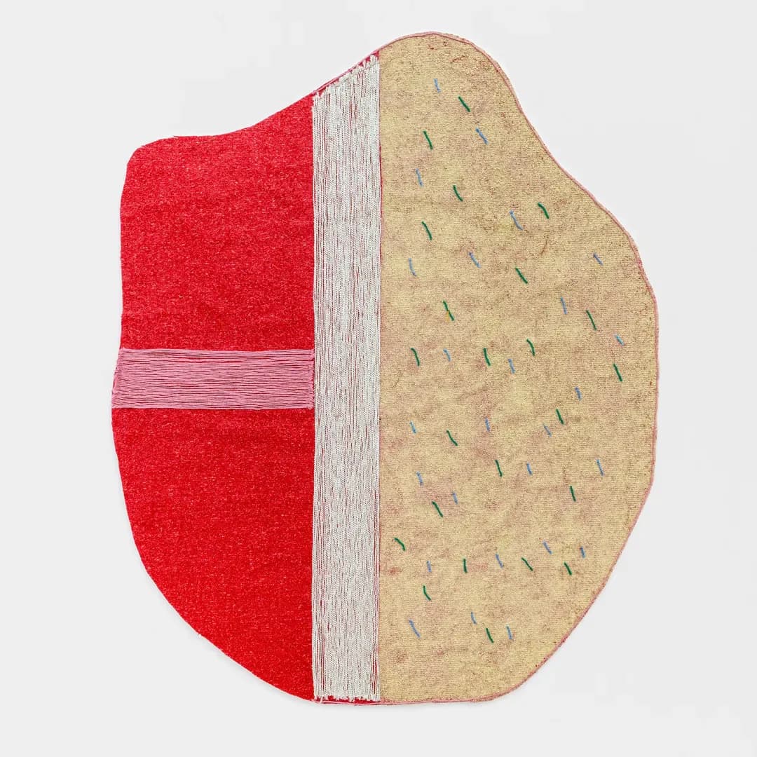 Mixed-media sculptural piece: oval form split vertically—red textured left half with white band, tan right half with green stitched marks.