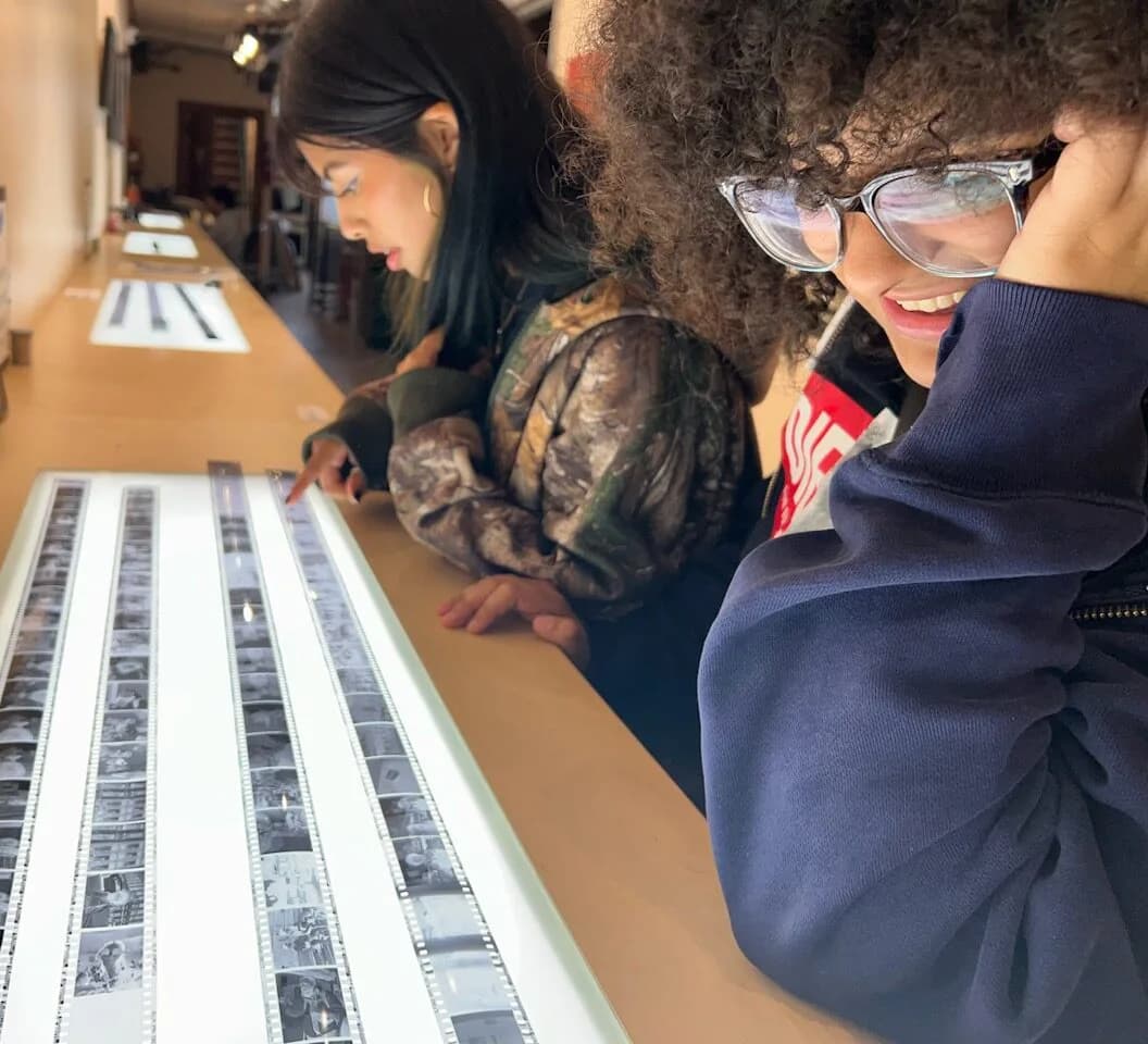 Visitors lean over a light table examining black and white film contact sheets at the Bronx Documentary Center