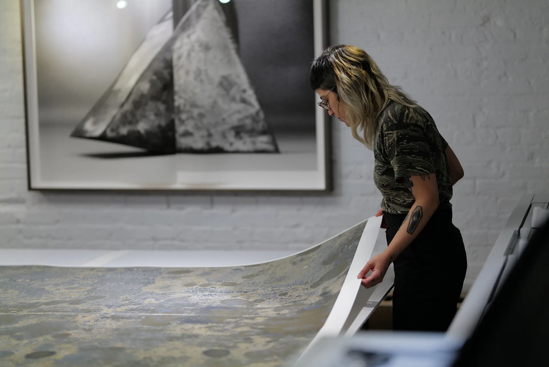 Gallery worker examining or handling a large textured artwork or fabric piece with mottled gray and white patina.