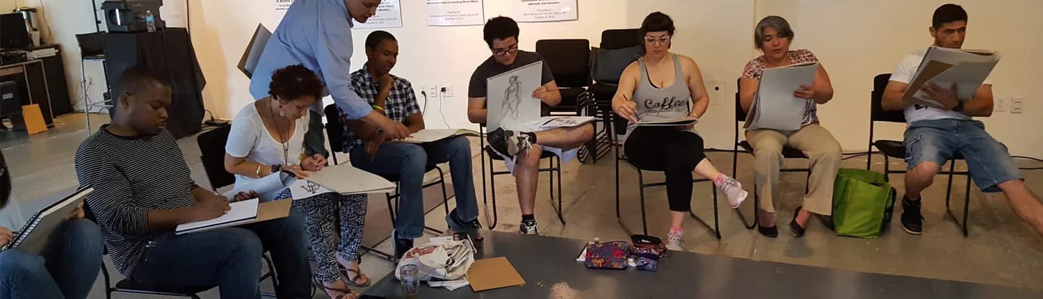Group of young people seated in circle in white-walled gallery space during workshop or discussion, with artwork visible on walls.