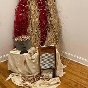 Gallery corner installation with draped cream and burgundy textiles, natural fiber materials, and a wooden washboard on wooden flooring.
