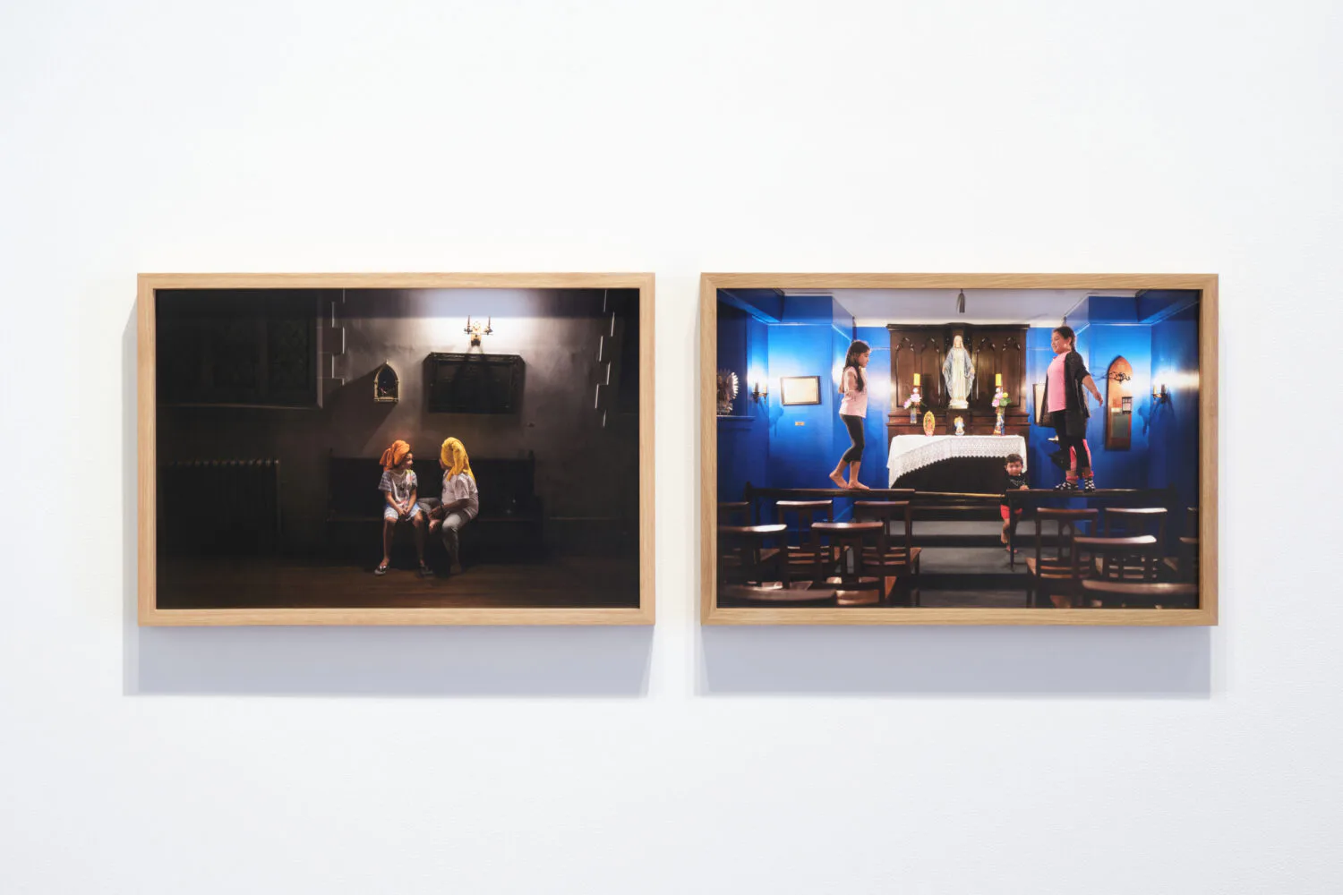 Two framed photographs side by side mounted on white wall; left shows dimly lit interior with two figures, right shows brightly lit stage scene with multiple figures in blue lighting.
