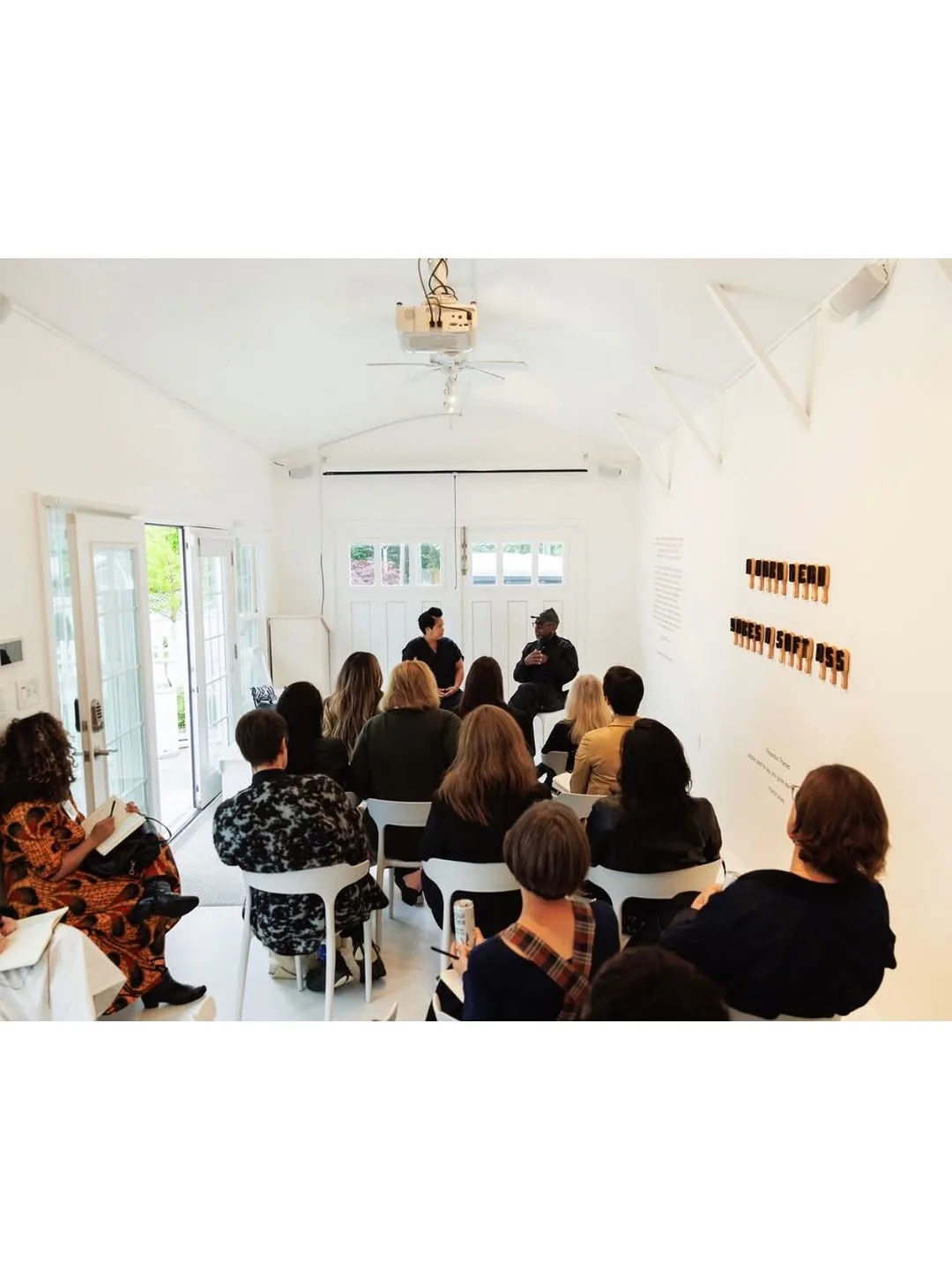 Interior of a bright white gallery space with vaulted ceiling where an audience sits facing two speakers near glass doors, hosted by the Center for Curatorial Leadership.