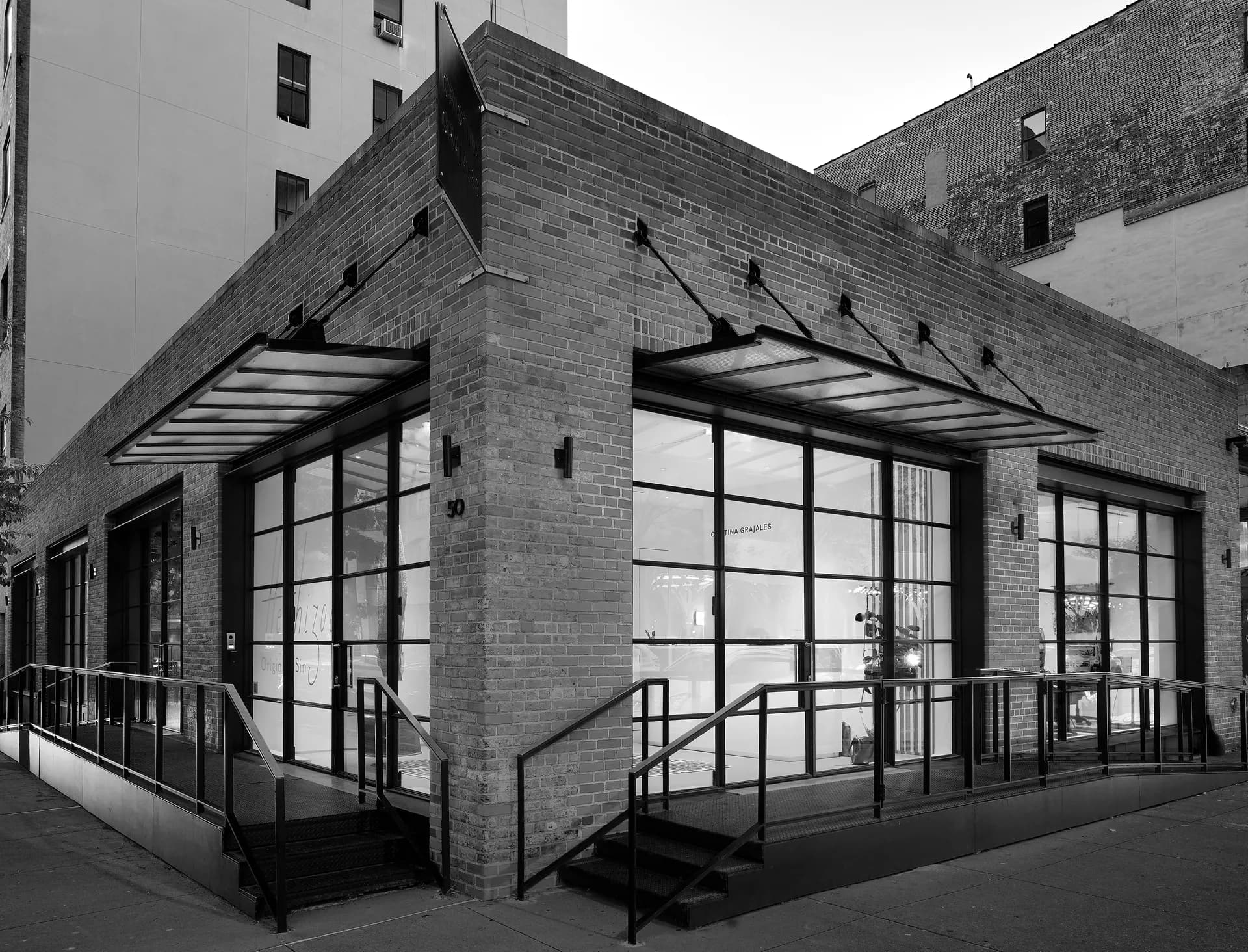 Exterior brick storefront of Christina Grajales gallery with large glass windows, metal awnings, and entrance stairs with railings