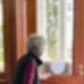 Woman standing by a sunlit window inside a wood-paneled room at the City Island Historical Society