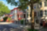 Brick townhouses on a tree-lined street in an urban neighborhood, including a red-painted building.