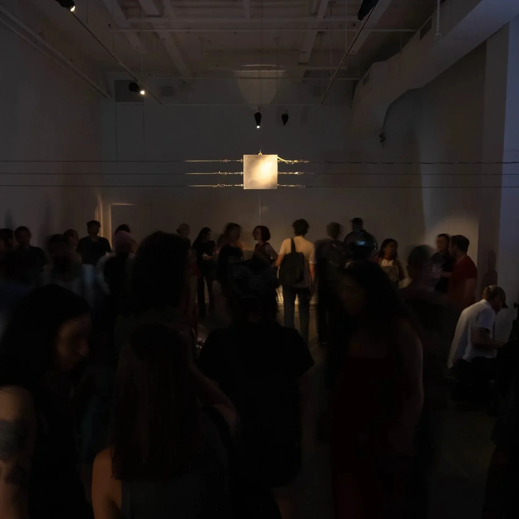 CUE Art Foundation gallery interior with visitors gathered around a glowing rectangular light installation suspended from the ceiling.