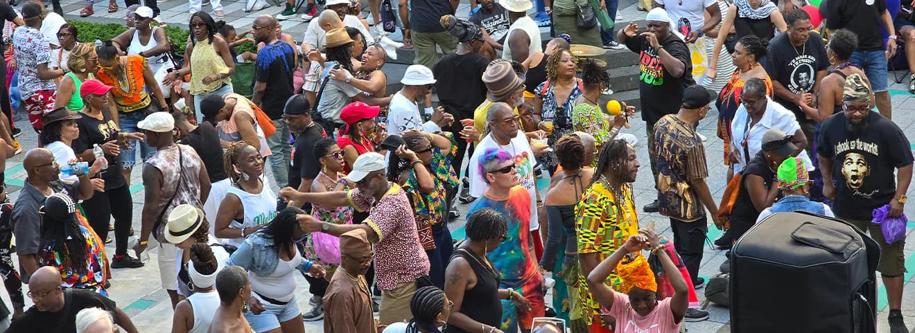 Crowded outdoor street festival with diverse attendees wearing colorful clothing and hats.