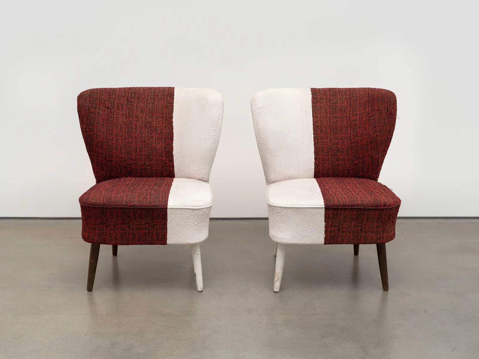 Pair of mid-century modern wingback chairs with two-tone upholstery in burgundy and cream fabric on wooden legs.