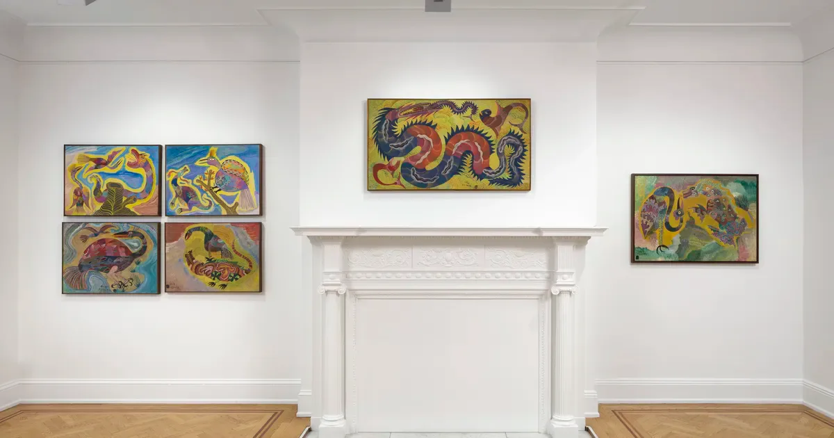 Bright gallery space with white walls and fireplace mantel displaying colorful abstract paintings in vibrant blues, yellows, and reds.