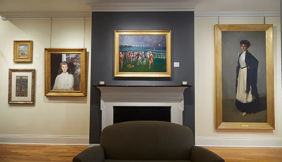 Gallery interior with a dark accent wall and fireplace mantel, several framed paintings, and a dark sofa in front