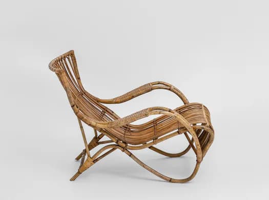 Sculptural bent-bamboo lounge chair with undulating curved form and woven rattan details, natural tan color on white background.