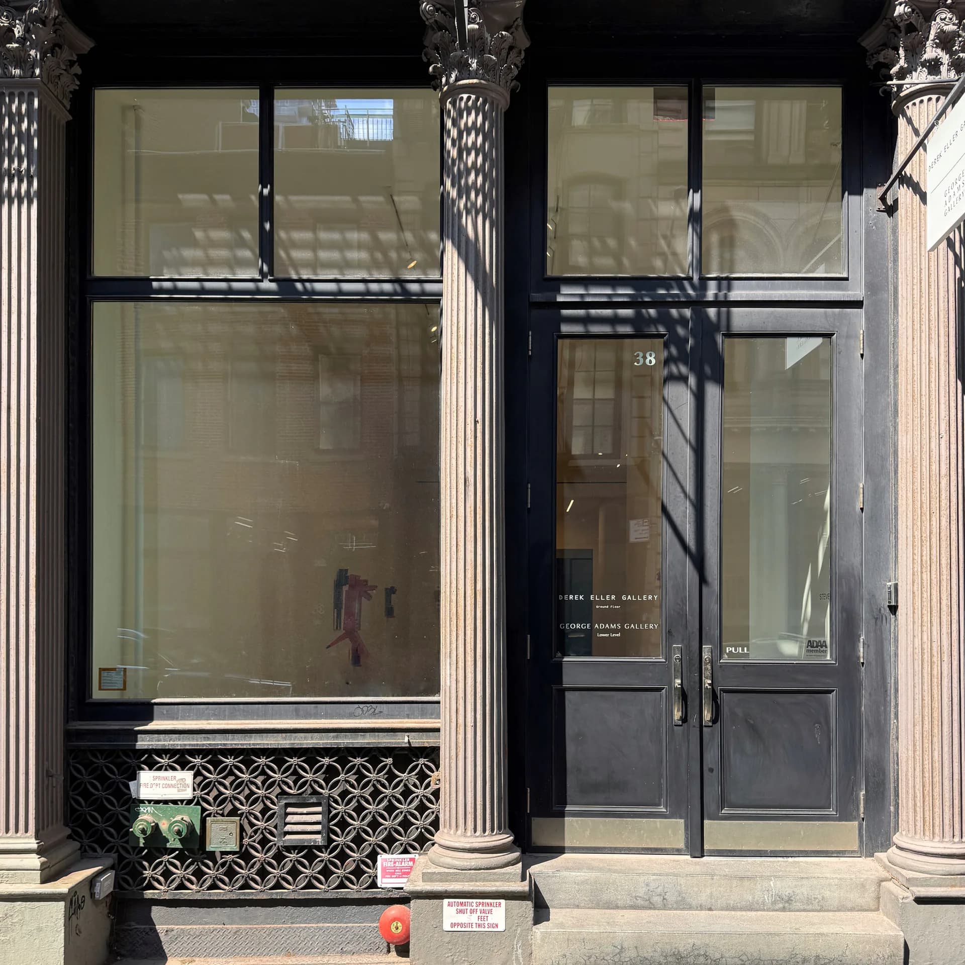 Storefront entrance of Derek Eller Gallery with black double doors, glass windows, and fluted columns