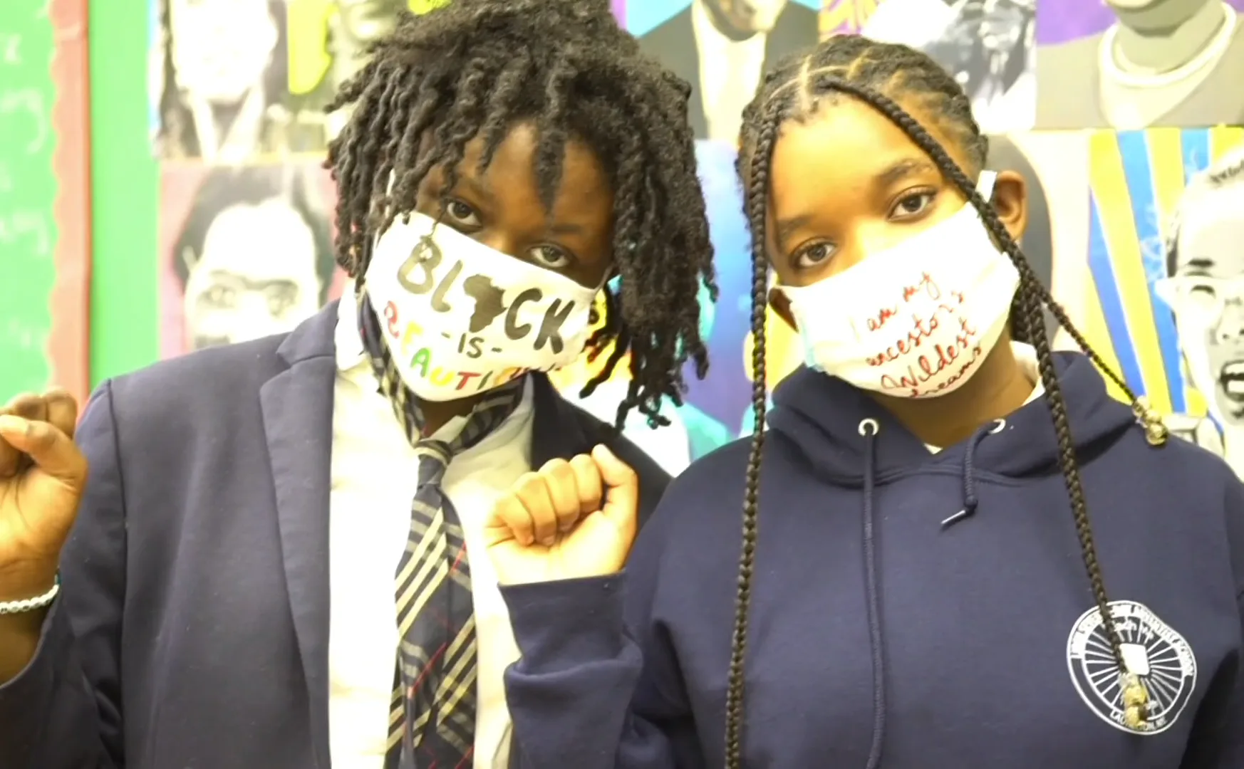 Two people holding fabric masks or signs with 'BLACK' text visible, wearing formal attire against colorful background, addressing social justice themes.