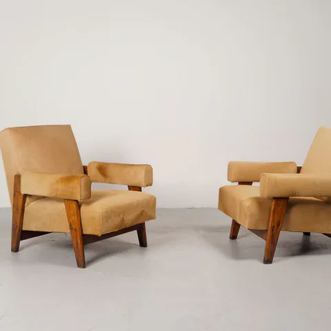 Pair of mid-century modern lounge chairs with tan leather upholstery, wooden frames in contrasting warm wood, and angular armrests on tapered legs.