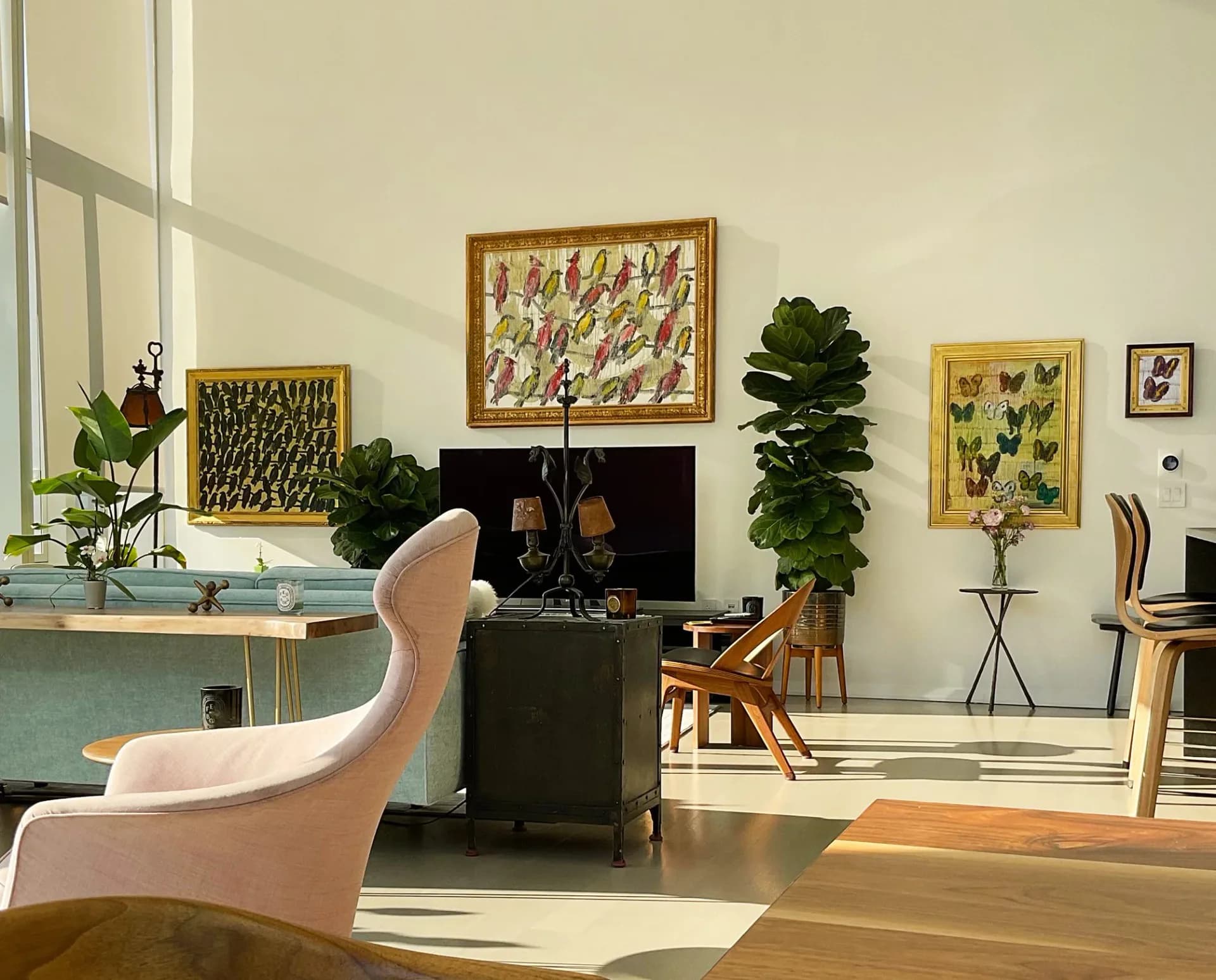 Modern gallery interior with curved cream chair, framed yellow butterfly and nature artworks on walls, houseplants, and minimalist furniture.