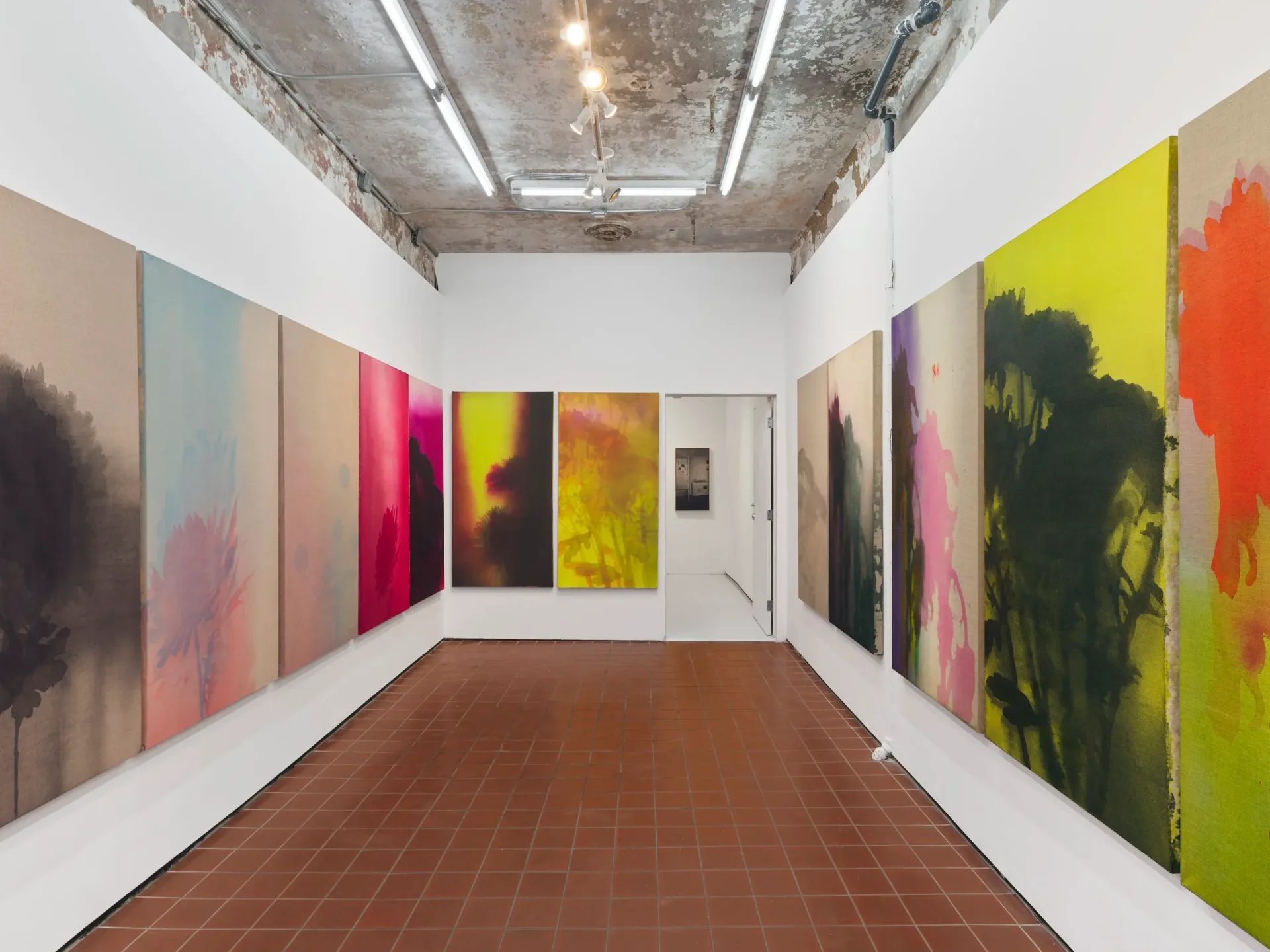 Gallery room with terracotta floor and large-scale abstract paintings in vibrant colors—yellow, red, pink, and green—covering white walls.