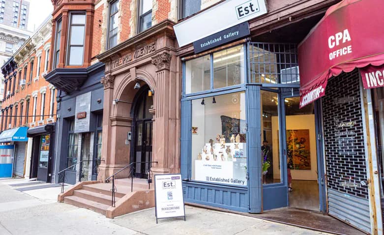 Storefront of Established Gallery with large glass windows displaying small sculptures, set within a brick building facade on a city street