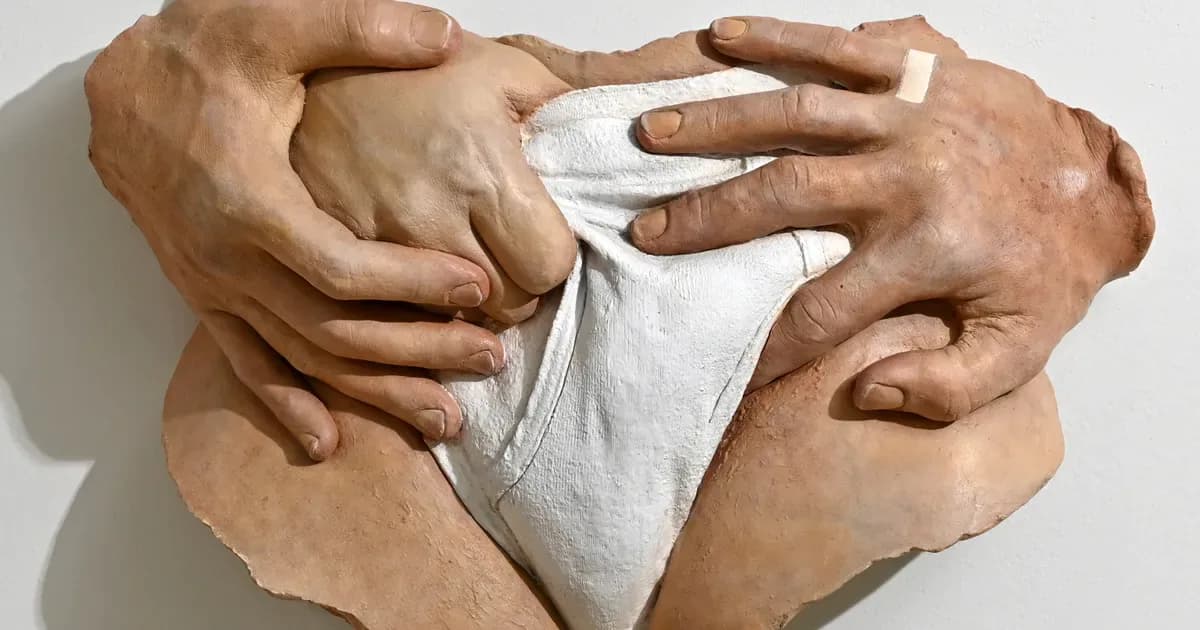 Sculptural hands in tan clay or resin cradling a white fabric object, mounted on white background.