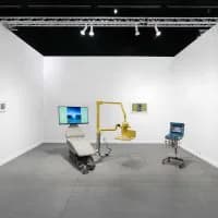 EUROPA gallery main space with minimalist white walls, gray floor, and displayed digital installations including screens and a yellow robotic apparatus.