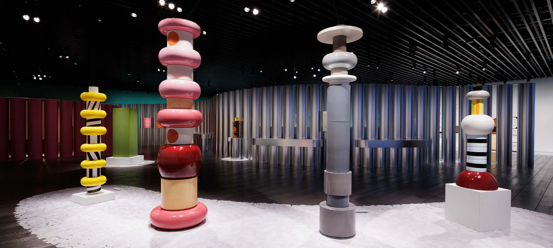 Gallery interior with industrial shipping containers and large sculptural cylindrical forms in red and gray.