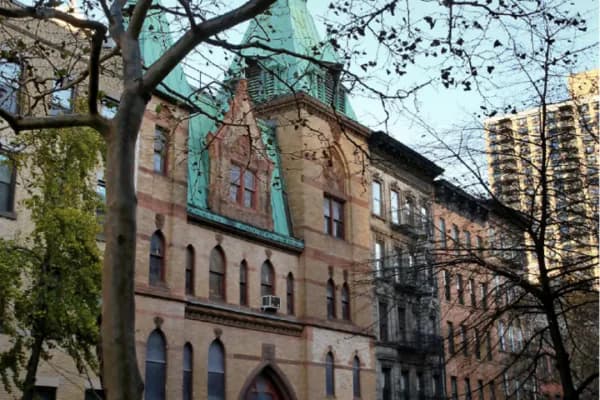 Photograph of row of historic red brick buildings with ornate stonework and large windows, flanked by bare tree branches and modern residential towers.