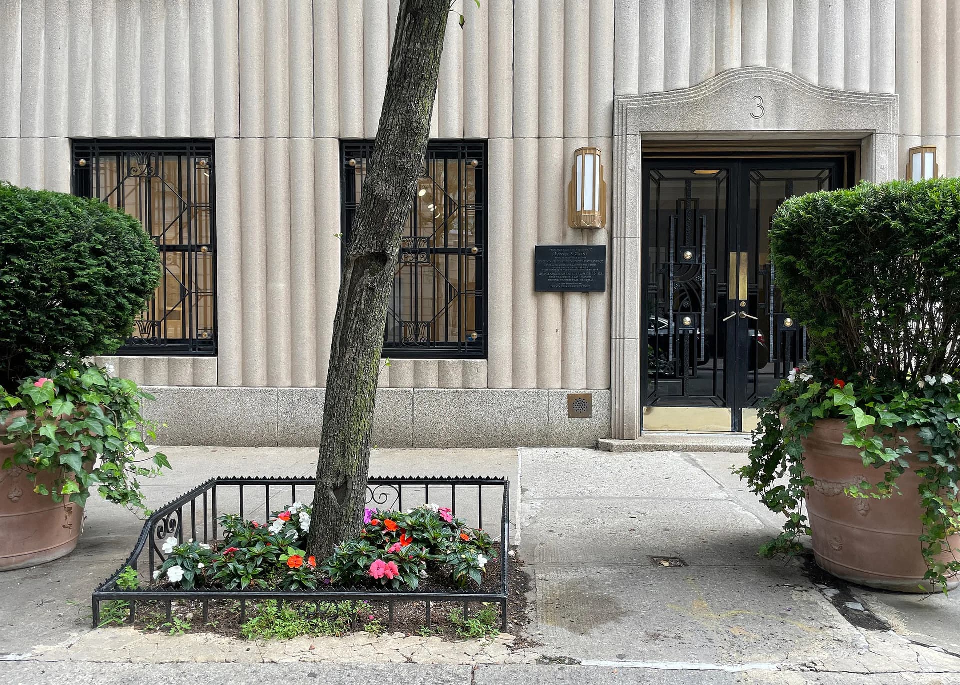 Exterior facade of Gitterman Gallery entrance with glass doors numbered 3, flanked by potted plants and a street tree