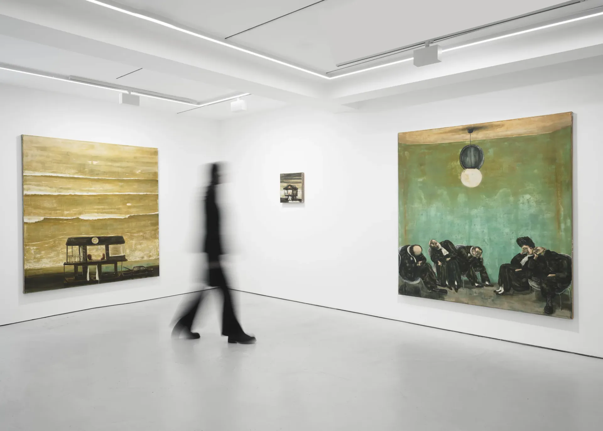 White gallery room with wooden floors, recessed ceiling lights, a figure in motion, and two large paintings depicting moody interiors and figures against colored backgrounds.