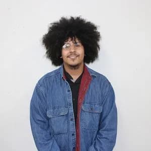 Portrait of person with black afro wearing denim shirt and red scarf against white background.