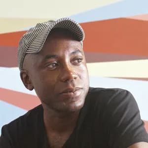 Portrait of person wearing black shirt and gray patterned beanie against colorful striped background wall.