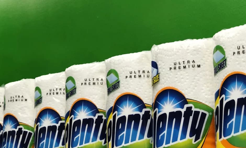 Close-up photograph of beverage bottles with bright blue starburst labels and white foam tops against a green background.