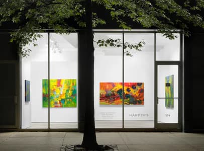 Harper's gallery exterior with colorful abstract paintings featuring yellow, orange, and red hues visible through glass storefront windows at night.