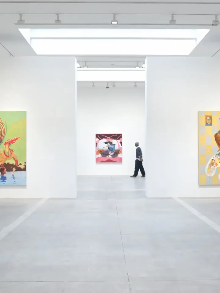 Minimalist Hauser & Wirth gallery interior with white walls, bright overhead lighting, and a person walking through the bright corridor viewing artworks.