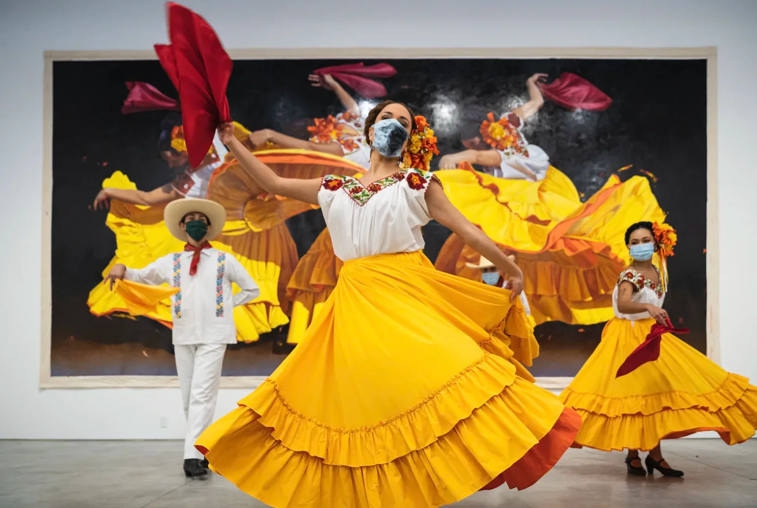 Colorful mixed-media installation featuring performers in vibrant yellow and red ruffled costumes against a large photograph with dramatic lighting and gestural figures.