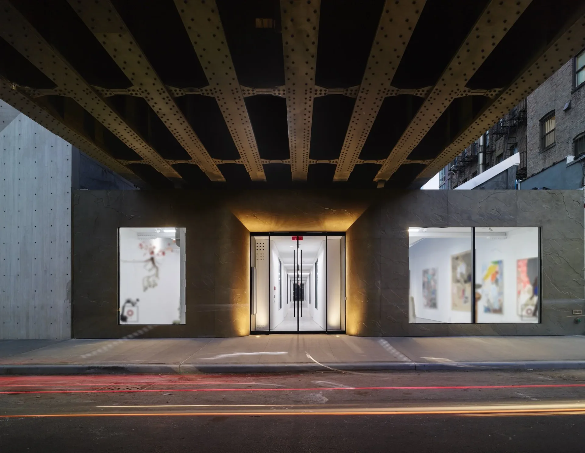 High Line Nine Galleries storefront exterior beneath concrete brutalist overhang, featuring illuminated window displays and dark facade with metallic entrance doors.